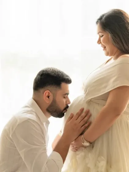 A tender moment captured with soft, natural light from a window. The father-to-be kisses the baby bump, creating a simple yet powerful image of love and anticipation.