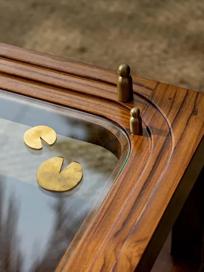 The beauty of our work is in the details. This close-up of our Kulam side table shows the custom-crafted brass elements that tell a story. Inspired by a tranquil Kerala temple pond, or 'kulam', these details depict lotus leaves and small figures, turning a simple table into a cherished memory.