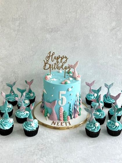 A mermaid-themed cake and cupcake set for Neeti's 5th birthday. The blue buttercream and pink mermaid tails create a beautiful underwater scene.