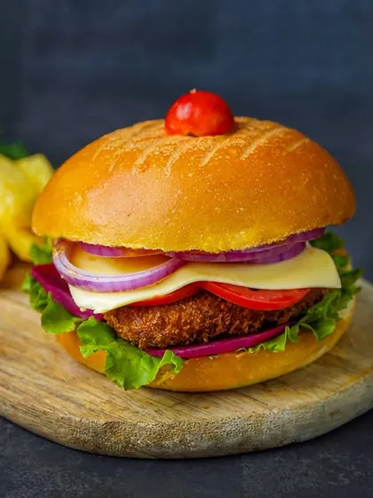 A close-up shot of a crispy chicken or veggie burger, focusing on the texture of the patty. The dark, dramatic lighting makes it look incredibly appetizing.