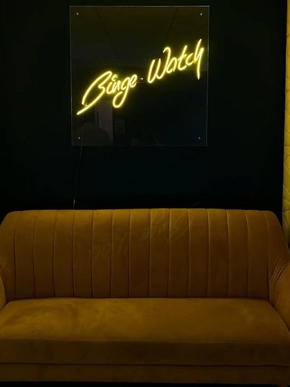 Our stylish waiting area featuring a comfortable sofa and our signature 'Binge Watch' neon sign. It's the perfect spot for a quick photo before your private screening begins.