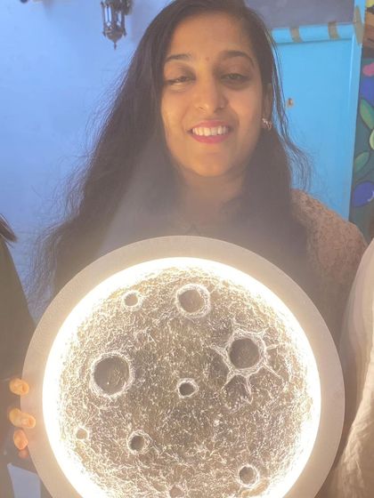 A participant smiles as she holds her glowing moon lamp, a testament to a fun and productive workshop session at the café.