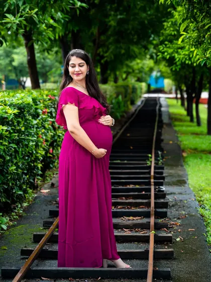 A beautiful solo portrait of the mom-to-be in a magenta gown, standing on a rustic railway track, symbolizing the journey ahead.