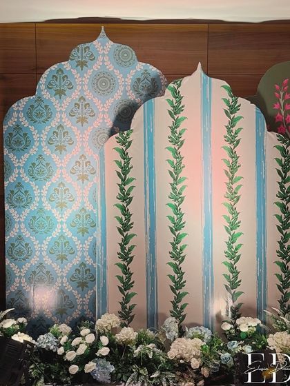 A beautiful backdrop created with custom-printed panels in shades of powder blue and green. The panels feature traditional Indian motifs and are flanked by arrangements of white and blue hydrangeas.