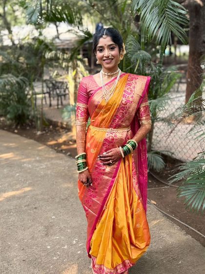 A full-length shot of the bride in her beautiful orange and pink saree. The makeup is flawless and perfectly suited for an outdoor, daytime wedding.