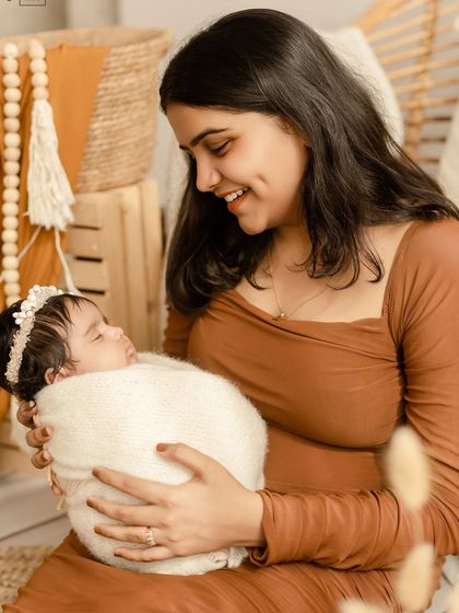 A new mother with a beautiful dimpled smile looks down at her sleeping baby. The earthy tones of her dress complement our boho studio decor.