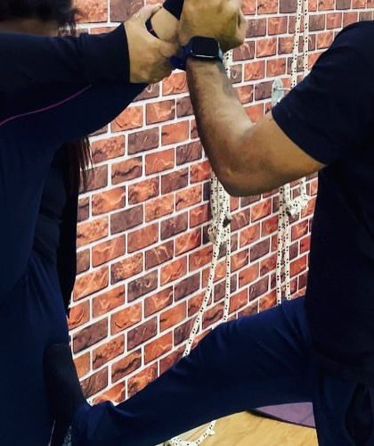 A student practices a standing split against the wall with instructor support, a great way to build flexibility and balance.