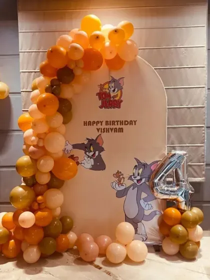 A Tom and Jerry themed 4th birthday with a custom arched backdrop and a balloon garland in muted orange tones.