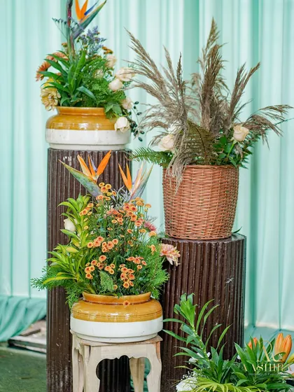 A rustic floral corner with arrangements in wicker baskets and ceramic pots, featuring pampas grass and tropical leaves.
