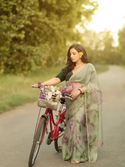 A picturesque moment on a country lane. The mother-to-be, in her elegant saree, stands with a bicycle adorned with flowers, creating a romantic and slightly vintage feel.