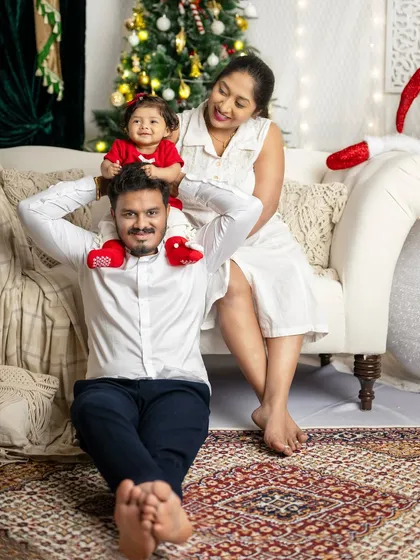 A playful moment between parents and their little one, who is sitting on her father's shoulders.