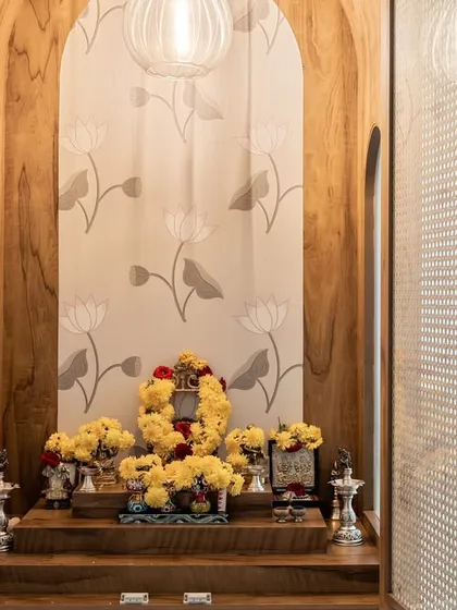 A serene pooja unit designed with natural wood and elegant rattan doors. The arched niche and lotus-patterned wallpaper create a peaceful and sacred space, beautifully integrating traditional elements into a modern home.