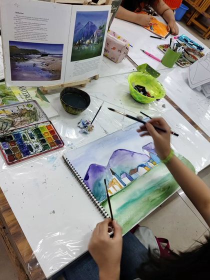 A teen student works on a scenic watercolor landscape, learning to create depth and atmosphere with washes of color.