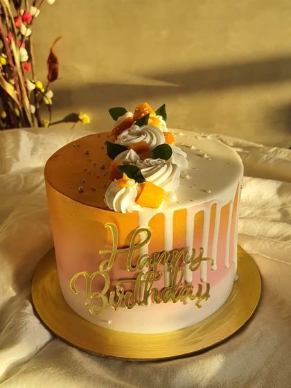 A beautiful mango birthday cake with a two-tone orange and pink ombre design, white chocolate drip, and fresh mango topping, all captured in the golden hour light.