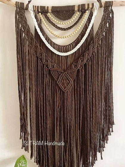 This large tapestry is made with rich chocolate brown cotton and features layers of white and beaded details. The wooden beads add a natural, earthy element to the design.