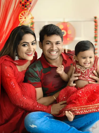 A candid moment of family joy during a Diwali celebration. This happy family of three shares a laugh, with their baby girl in a festive red outfit, perfectly capturing the real, unfiltered smiles we love to photograph.