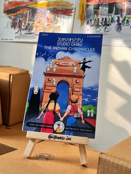 The calendar cover displayed on its wooden easel. It's designed to be a beautiful and functional piece of desk art.