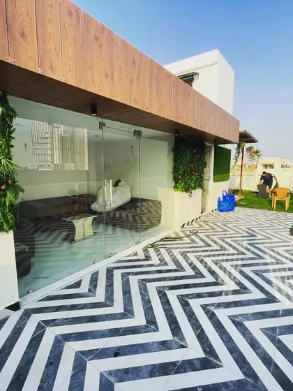 A wider perspective of the Janakpuri terrace, showing the seamless integration of the glass-enclosed seating area with the open-air lawn and modern flooring.
