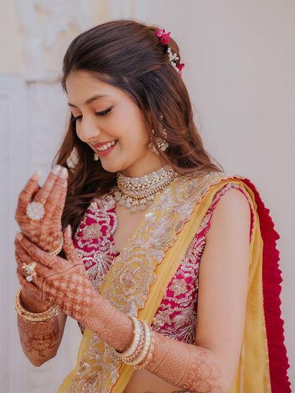 A soft and romantic Haldi look. The makeup features pink tones that complement her yellow and pink lehenga, with her hair adorned with fresh flowers.