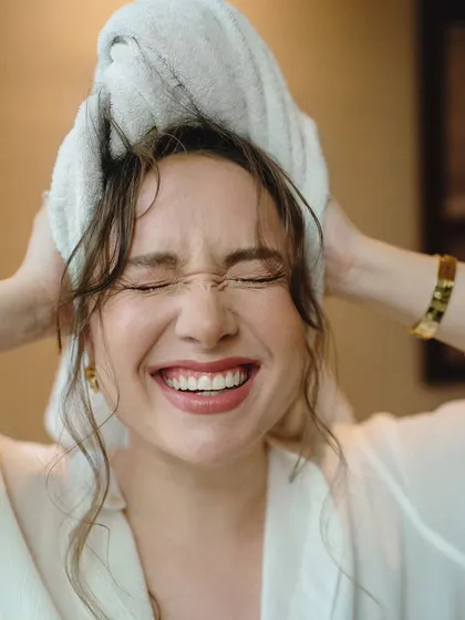 A candid moment of pure joy from a cinematic portrait session. The model's spontaneous laughter while drying her hair creates an authentic and relatable image.