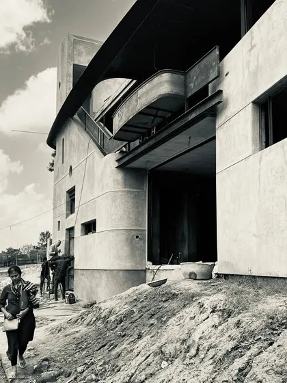 A view of the south side of a project under construction. The black and white photograph emphasizes the building's form, texture, and the human scale against the raw structure.