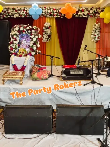 The main stage decoration for a Bhagwat Katha, featuring a floral frame around the deity's picture, with simple balloon clusters and a draped backdrop.
