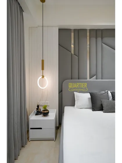 A detail of the bedside in the Tata LaVida guest room. The combination of the grey quilted headboard, the vertical fluted panel, and the modern ring-shaped pendant light creates a chic and contemporary look.