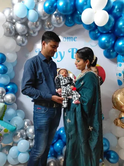 The proud parents with their newborn in front of the welcome home decor. The blue, white, and silver color scheme is a classic choice for celebrating a baby boy.