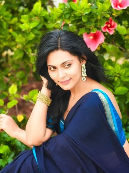A beautiful portrait amidst flowers and greenery. The natural setting enhances the elegance of the blue saree.