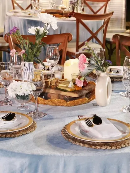An elegant table setting for a communion dinner. The light blue tablecloths, wooden cross-back chairs, and floral centerpieces create a serene and sophisticated atmosphere.