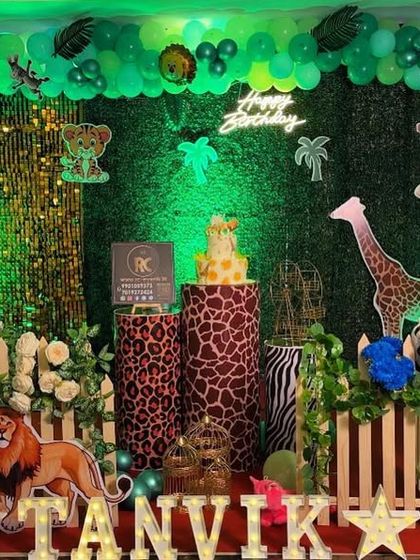 An immersive jungle theme with green lighting and a dense foliage backdrop. This setup features multiple animal cutouts, animal-print plinths, and a personalized photo of the birthday boy.
