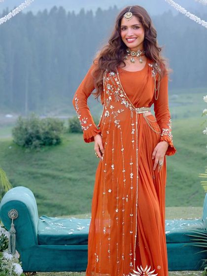 A full shot of the model in the burnt orange outfit, showcasing its unique drape and design in a beautiful outdoor setting.