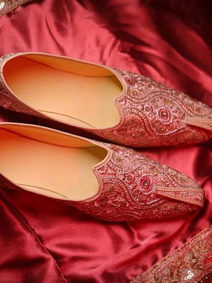 A close-up of the groom's traditional shoes (juttis) on a rich, red fabric.
