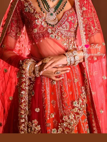 A detailed shot focusing on the bride's hands, adorned with intricate kadas and rings, complementing the heavy embroidery of her lehenga.
