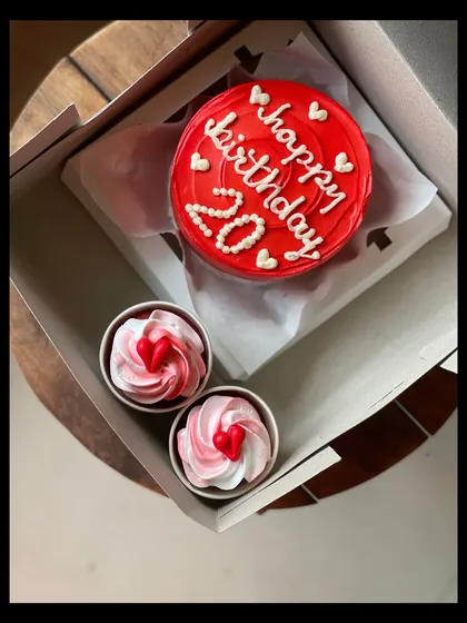 A vibrant red bento cake for a 20th birthday, paired with two pretty pink and white swirled cupcakes. The tiny hearts on all the treats make it an extra sweet gift.