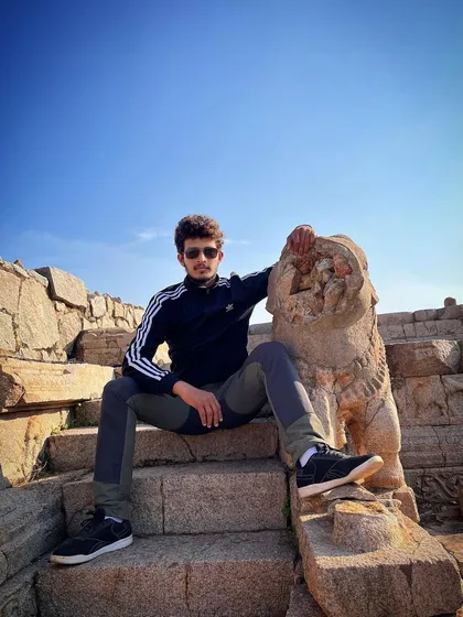 Exploring the historic, rocky terrain of Hampi. Posing with a stone lion statue on the steps of an ancient temple.
