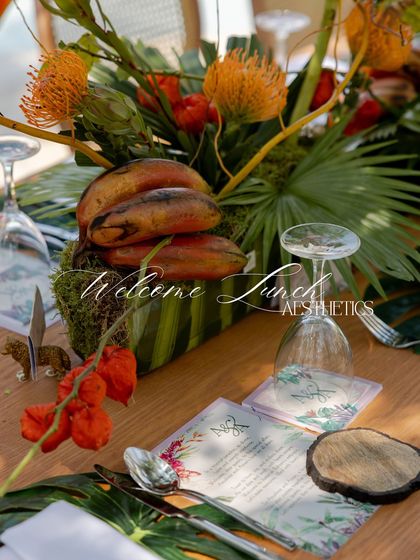 A close-up of the 'Welcome Lunch' aesthetics. The menu card, wooden coaster, and unique floral arrangement with cacao pods create a highly detailed and thematic setting.