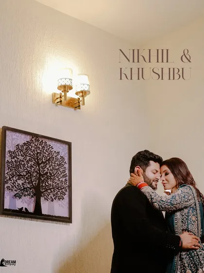 An intimate portrait of Nikhil and Khushbu, their foreheads touching, set against a simple, artistic backdrop in their home.