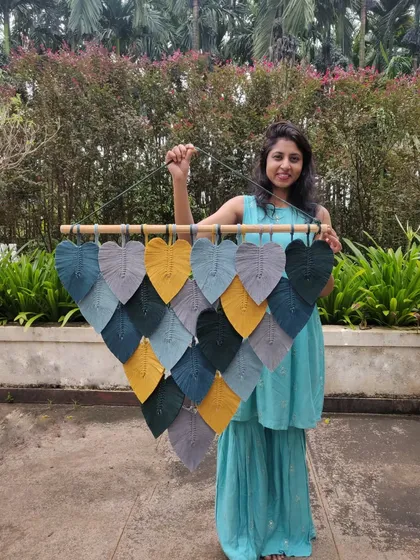 The colors in this photo blend so beautifully. Holding our macrame leaf wall hanging against a lush green background highlights the mustard, grey, and teal tones of the piece.
