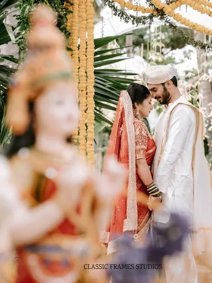 A serene and spiritual moment between the couple at their wedding ceremony. The blurred traditional figurines in the foreground add a unique cultural and artistic layer to the photograph.