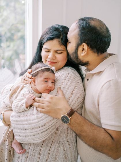 A father's gentle kiss on his wife's forehead as she holds their baby. A beautiful moment of connection and shared joy.