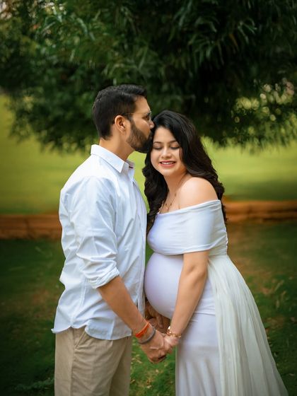 A simple and sweet moment of love. The partner's gentle kiss on her forehead in a green park setting perfectly captures the tenderness of this time.