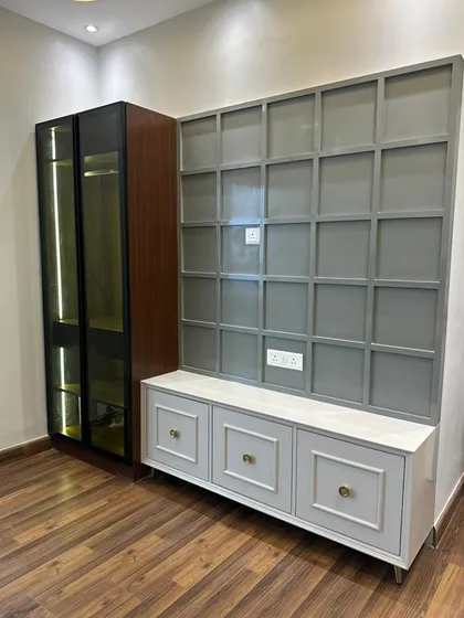 This custom TV unit combines a gridded grey panel feature wall with a low-profile white cabinet. To the side, a dark wood and glass display cabinet with internal lighting provides a beautiful space to showcase decor items.