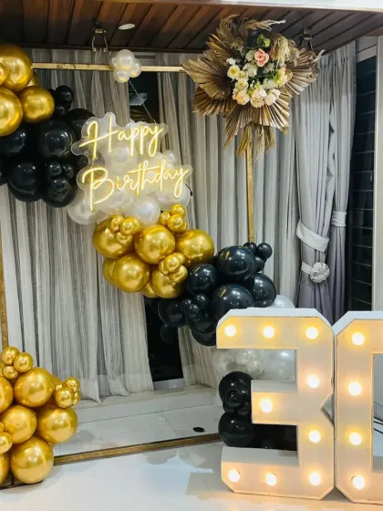 Celebrating a 30th birthday with style. This chic setup features a modern gold, black, and white balloon arrangement on a metal frame, a custom 'Happy Birthday' neon sign, and large marquee numbers, creating a sophisticated photo corner for the party.