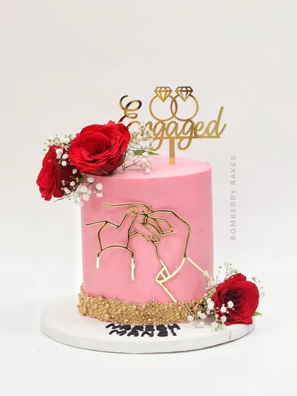 A vibrant pink engagement cake with a modern gold wire art topper, fresh red roses, and a gold sequin base.