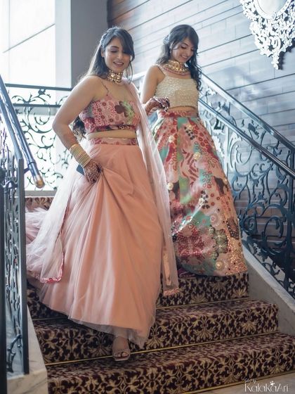 The bride and her sister or bridesmaid descending a grand staircase together. A lovely candid moment showing sisterly love and support.