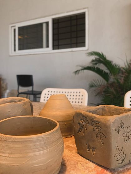 A collection of raw, unglazed pieces on the studio table, including a pot with leaf carvings.
