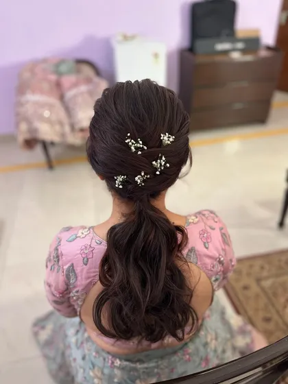 A messy ponytail with a textured crown and delicate baby's breath flowers tucked in. This is a romantic and soft look, perfect for an engagement.