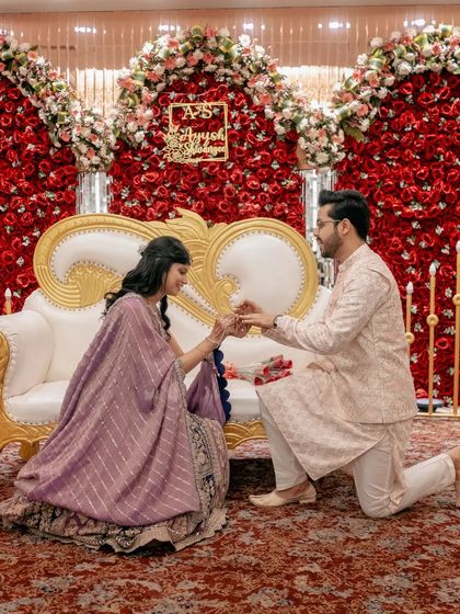 A beautiful, wide-angle shot of the proposal against a stunning wall of red roses, capturing the grandeur of the moment.
