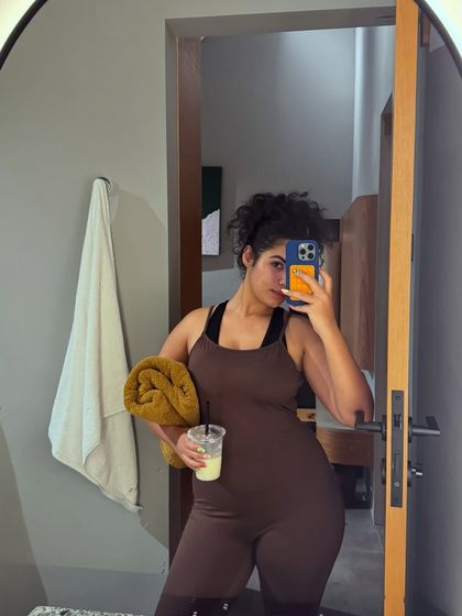 A mirror selfie in a brown workout jumpsuit, holding an iced drink. This is a casual, behind-the-scenes moment from my vacation.